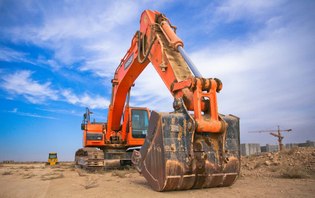 pexels-photo-1078884-1078884 A large orange excavator working on a construction site under a blue sky.