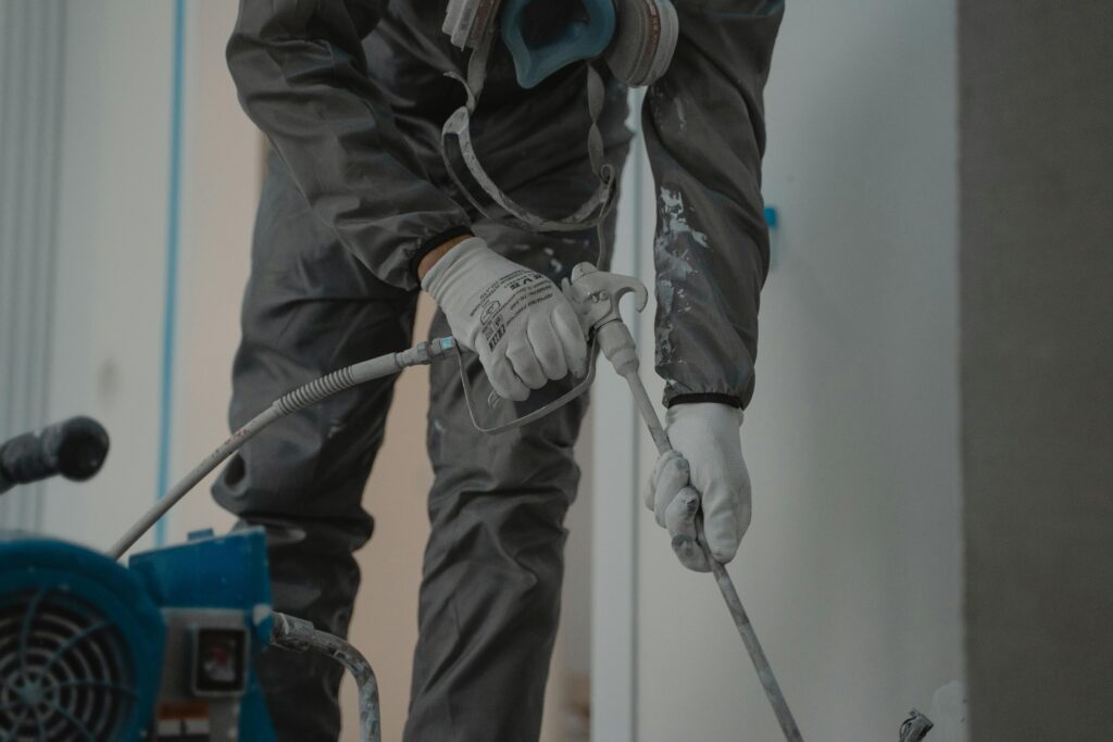 pexels-photo-6474193-6474193 Worker in protective gear using a power spray for indoor renovation.